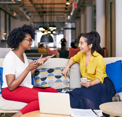 African-American and Asian women talking in work lounge area
