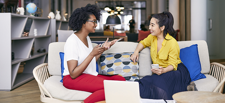 African-American and Asian women talking in work lounge area