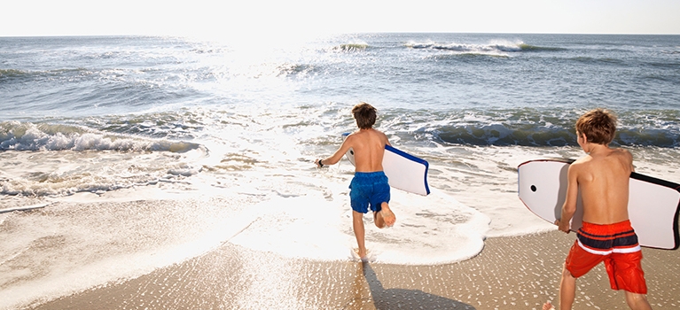 Two boys running into ocean with bodyboards