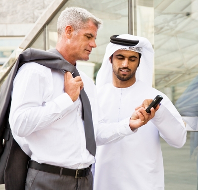 Caucasian businessman and an Arabic male colleague reading something on a cell phone.