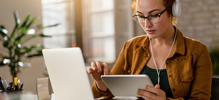Young creative businesswoman working on digital tablet while wearing headphones in the office. 
