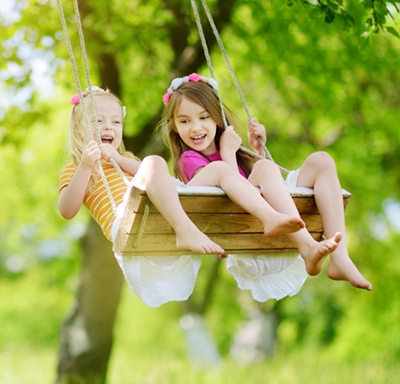 Two young girls swinging together on a tree swing