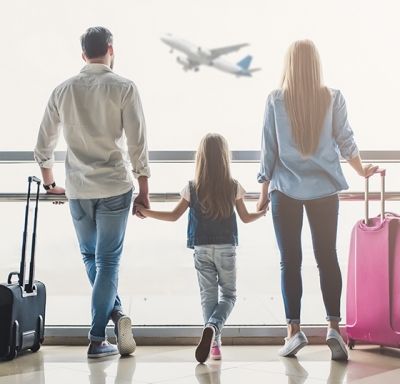 Parents and daughter holding hands at an airport while watching a plane take off