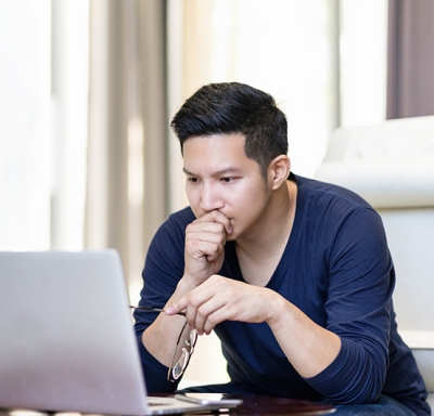 Man holding glasses and reading off his laptop