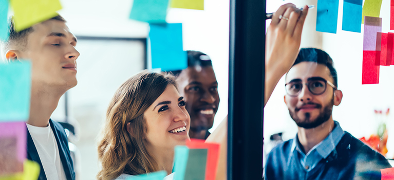 Young coworkers brainstorming while woman writes notes on post-it note 