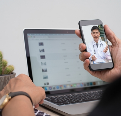 Woman talking to doctor on smart phone with laptop open in background