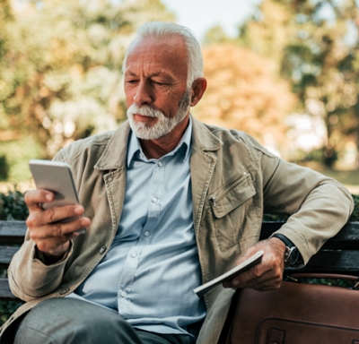 Senior male with beard looking at phone on park bench