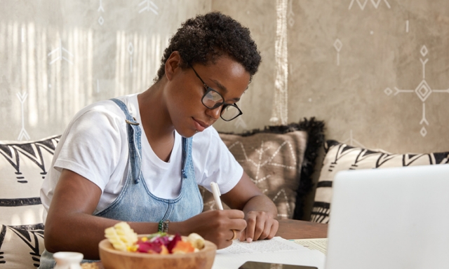 African-American woman writing at a restaurant table while working, with a bowl of food nearby