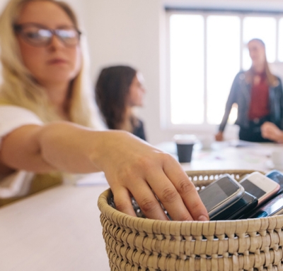 Woman placing mobile phone in basket with other phones