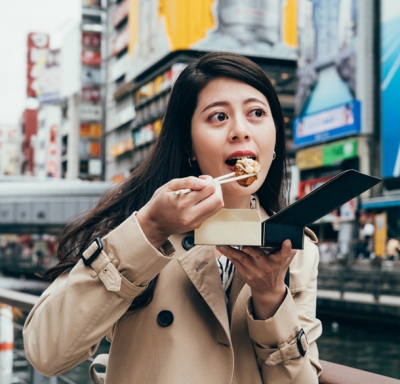 Japanese businesswoman eating takoyaki in the dotonbori in Osaka, Japan.