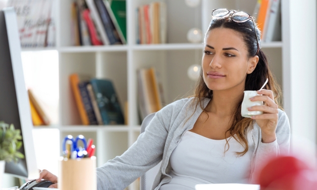 Woman eating yogurt and checking email while working in her home office