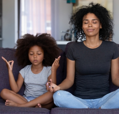 African-American mother and daughter meditating on a sofa
