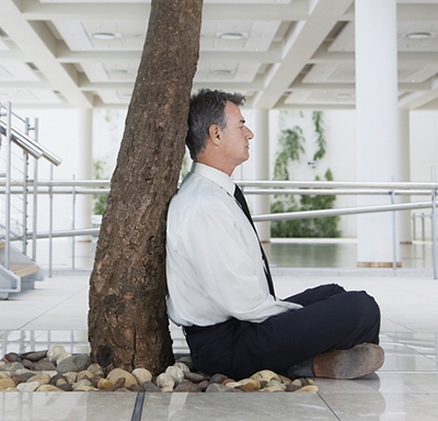 Businessman meditating under a tree in an office building