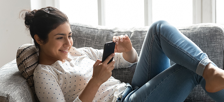 Young woman using cell phone on living room sofa