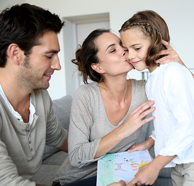 Mother kissing her daughter while the father looks at the picture the daughter drew for her mother