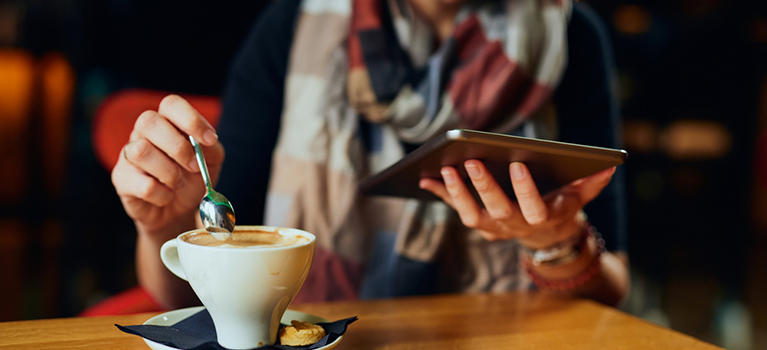 Beautiful Caucasian woman with coffee looking at her tablet	