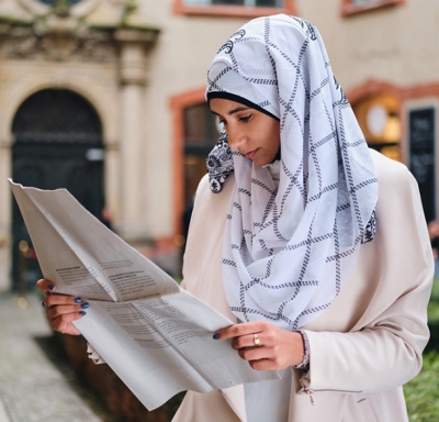Woman in hijab reading newspaper on a city street