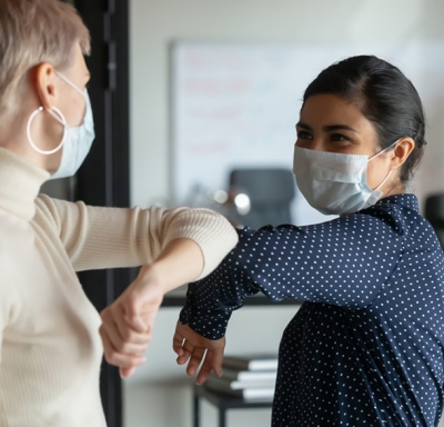 Female colleagues wearing protective face masks and bumping elbows at work