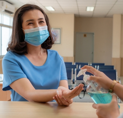 Patient with mask getting hand sanitizer from worker in medical office