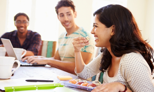 Young woman eating sushi at lunch as her co-workers sit nearby