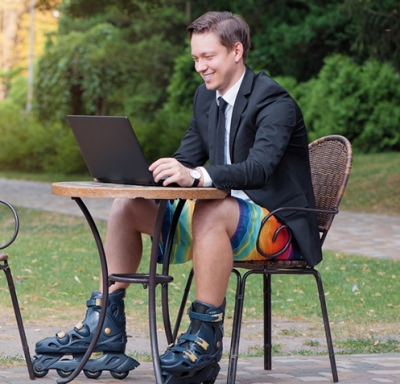 Businessman in suit jacket and tie, shorts and skates working on laptop outdoors