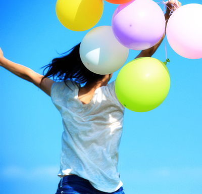 Young woman holding balloons while jumping in celebration