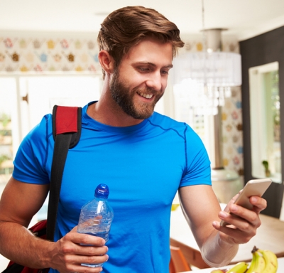 Caucasian male holding water bottle and looking at phone in his kitchen