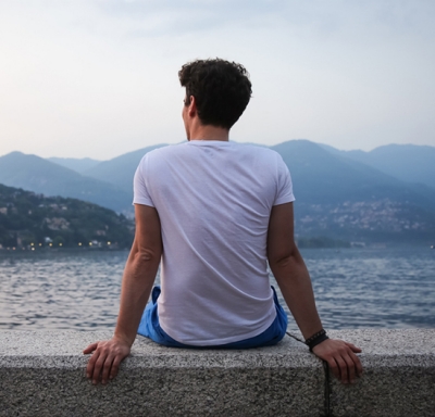 Athletic young man seated on a wall looking out at a lake and mountains