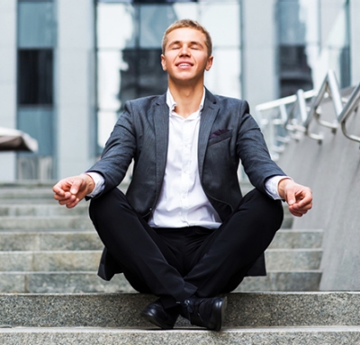 Young businessman meditating on steps outside of office building