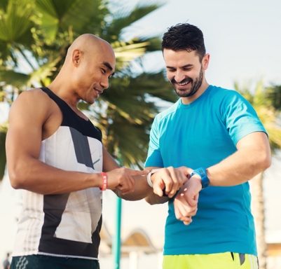 Male friends comparing smartwatches after a workout in a Dubai park