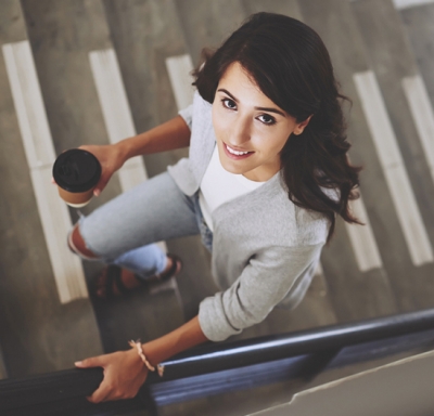Brunette female walking up stairs, looking up while holding a cup