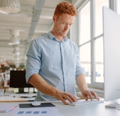 Young redheaded man standing at desk in front of computer