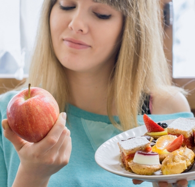 Woman looking at an apple while holding a plate of pastries