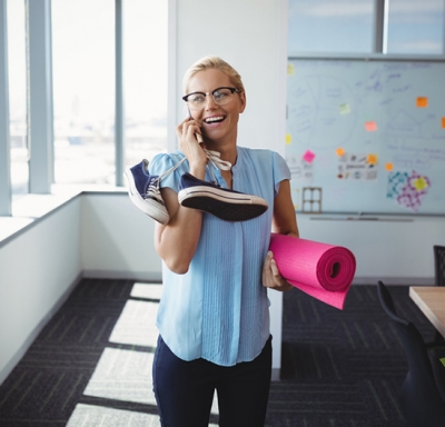 Businesswoman carrying yoga mat and sneakers while talking on cell phone