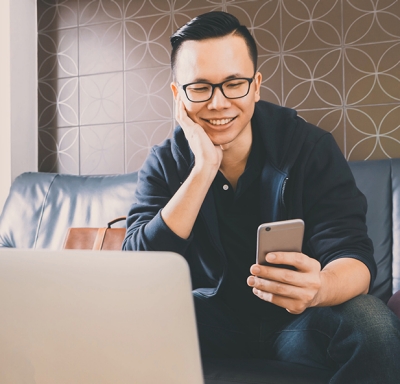 Asian businessman checks phone with laptop in front of him