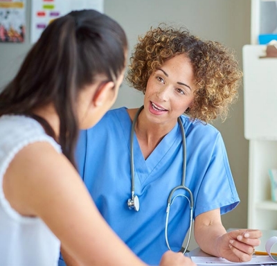 Female doctor sits at her desk and listens to a female patient