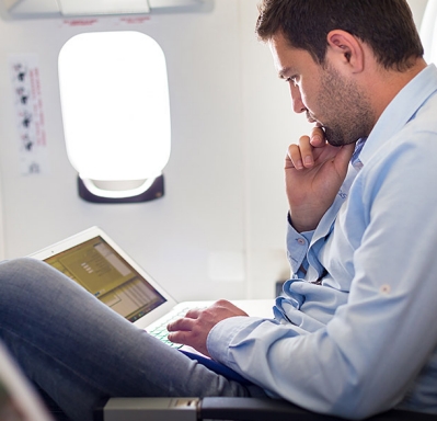 Casually dressed middle aged expat man working on laptop in aircraft cabin during his business travel. 