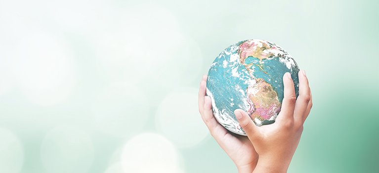 Two human hands holding earth globe over blurred nature background. 
