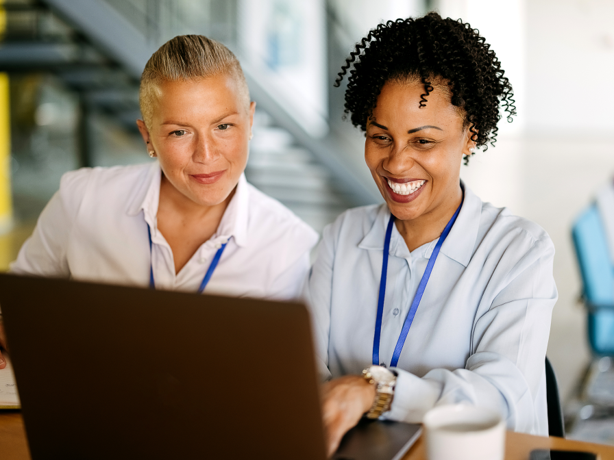 Two women smiling while looking at a laptop.