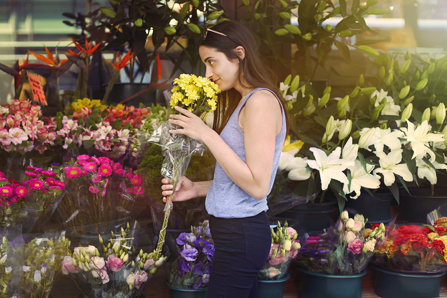 A photo of a woman at the market, taking the time to smell the flowers