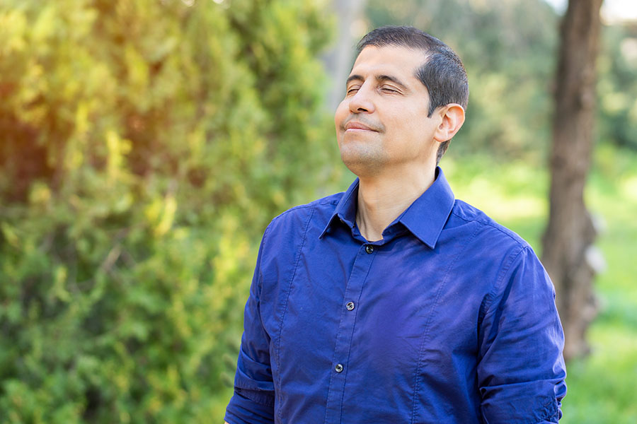 man taking a deep breath surrounded by trees