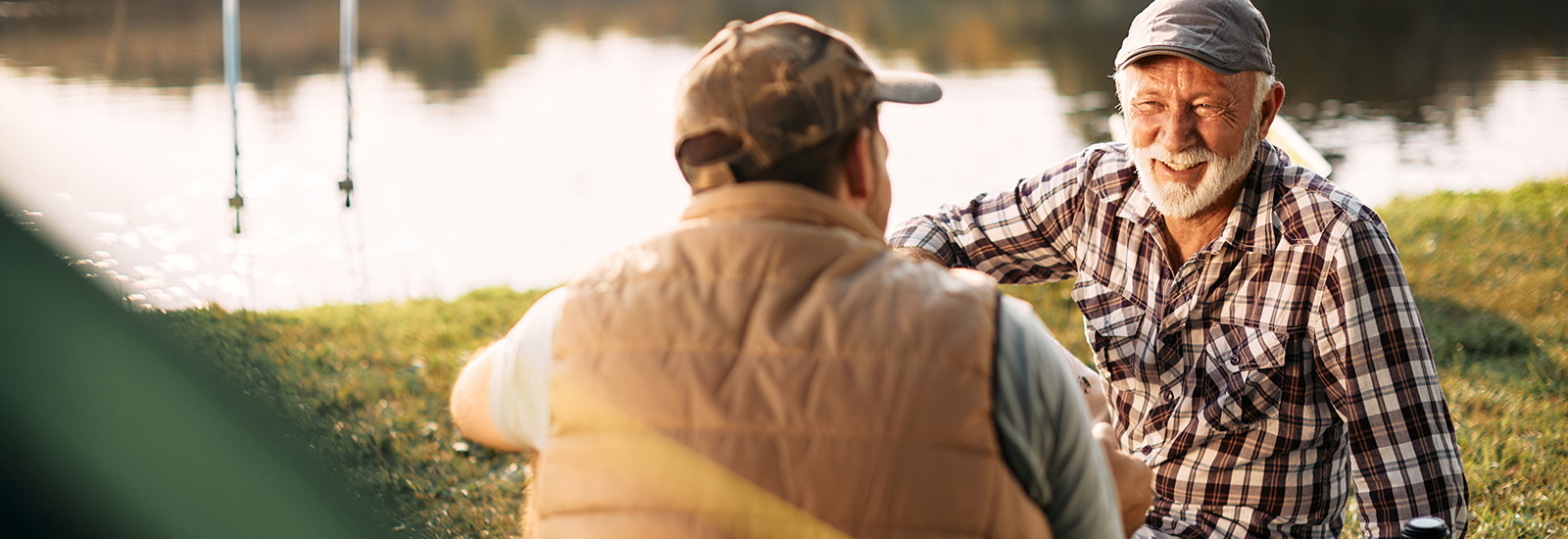 Happy mature man and his son enjoying in conversation while fishing during their camping day.