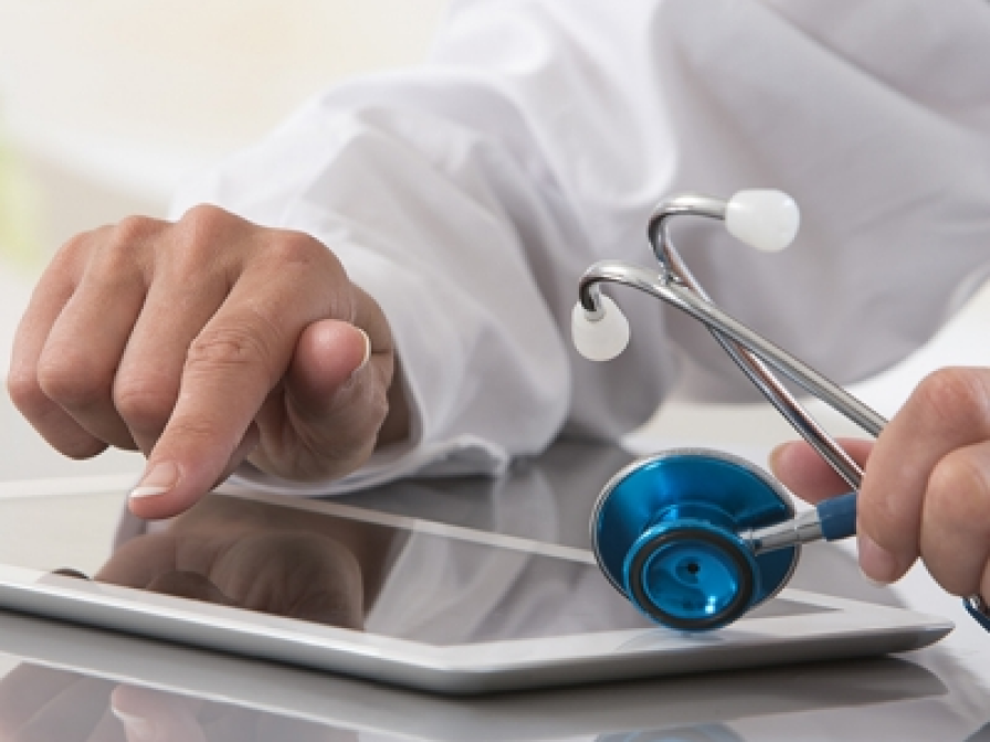 A close-up of a person using a tablet while holding a stethoscope