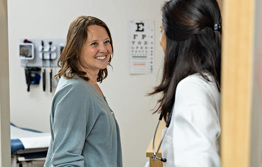 Woman walking into a doctors office and smiling at her care provider